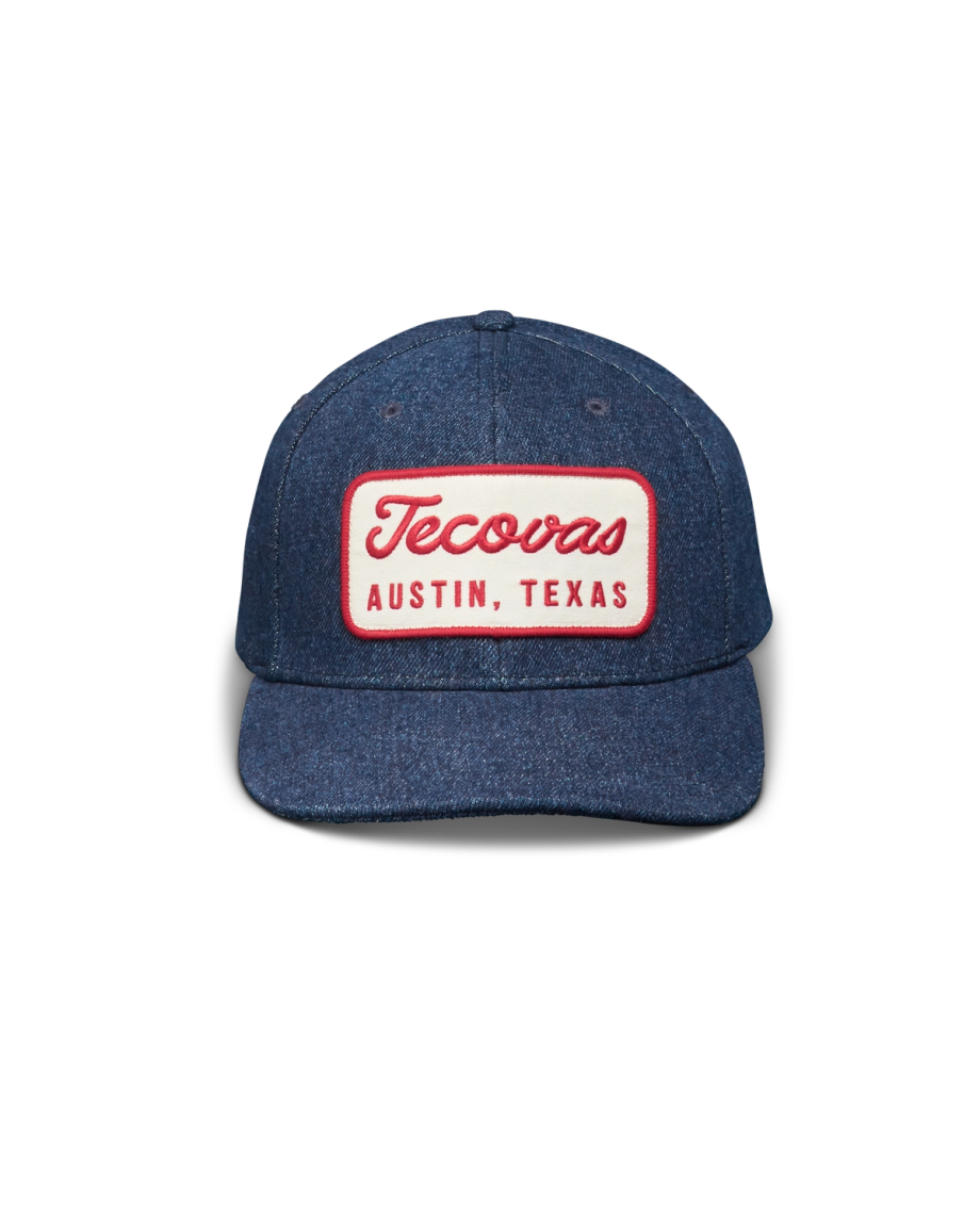 A blue denim baseball cap with a red and white patch that reads "Tecovas Austin, Texas" on the front.