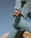 A person wearing a light blue denim shirt and jeans is climbing over a rock, with one hand visible and the sky in the background.