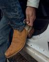 A person in jeans stepping onto a vehicle step, adjusting the sock inside a worn brown cowboy boot.
