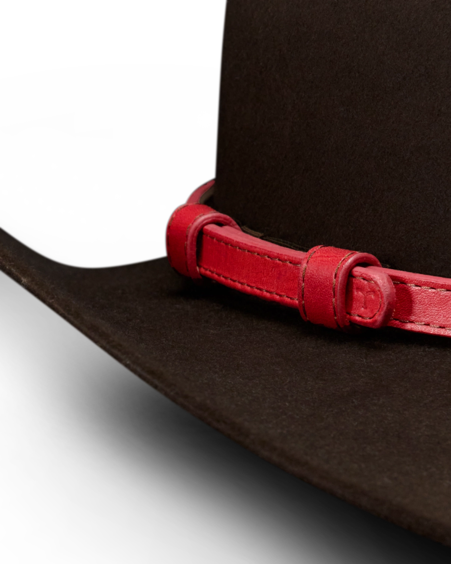 Close-up of a dark brown hat with a wide brim, featuring a red leather band wrapped around the base of the crown.