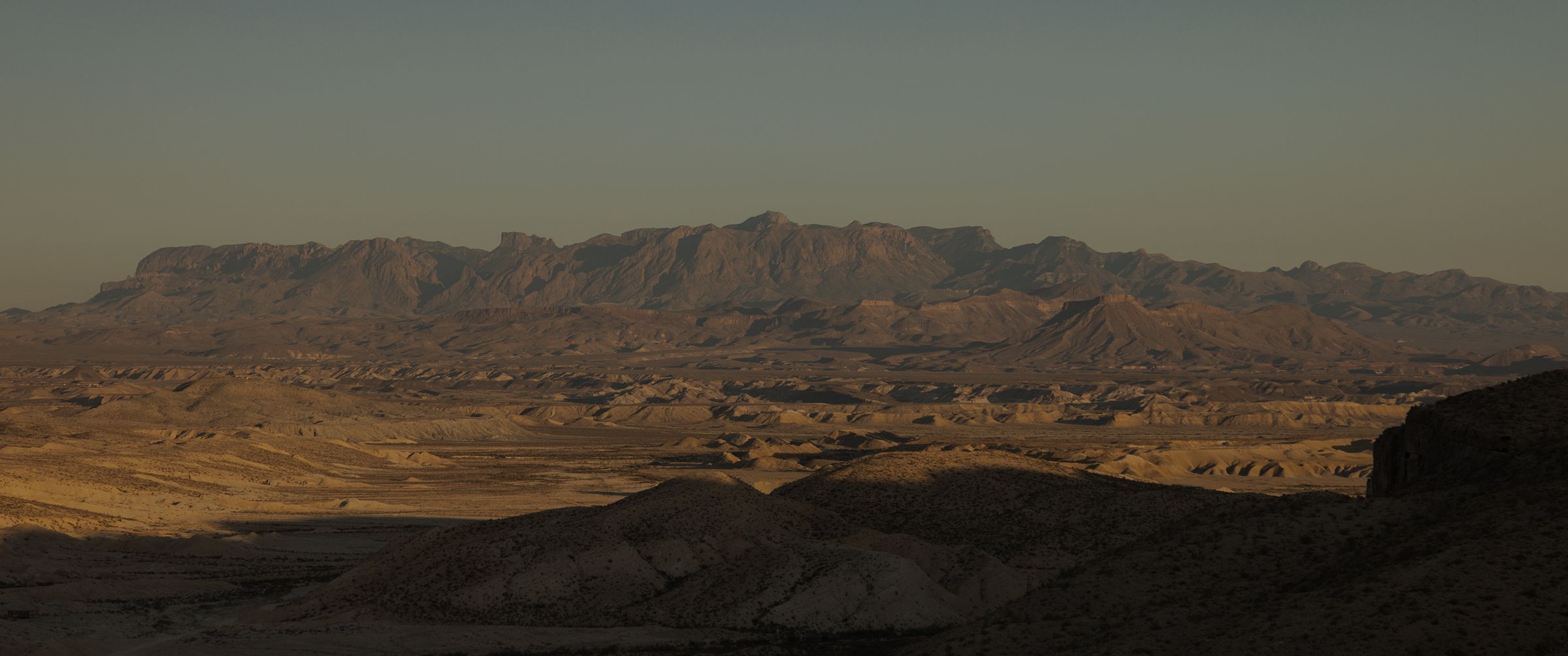 Panoramic view of a vast desert landscape with rolling hills and distant rugged mountains under a clear sky.