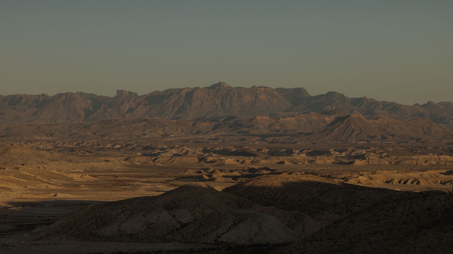Panoramic view of a vast desert landscape with rolling hills and distant rugged mountains under a clear sky.