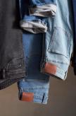 Three pairs of jeans, including black, medium blue, and light blue, are hung side by side with visible brown leather patches and rolled-up cuffs.