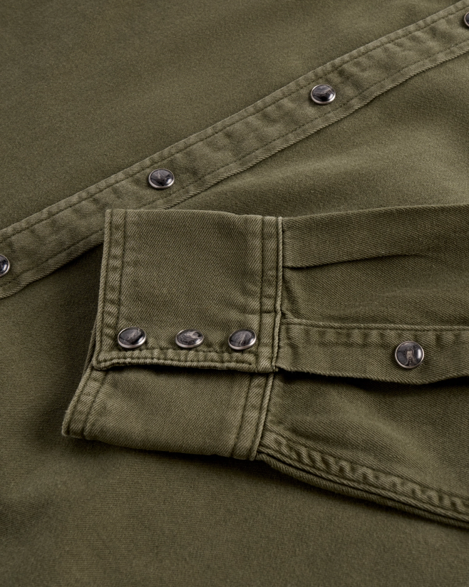 Close-up of an olive green denim shirt with dark, marbled snap buttons on the placket and sleeve cuff.