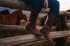 woman wearing tecovas cowgirl boots on a ranch fence