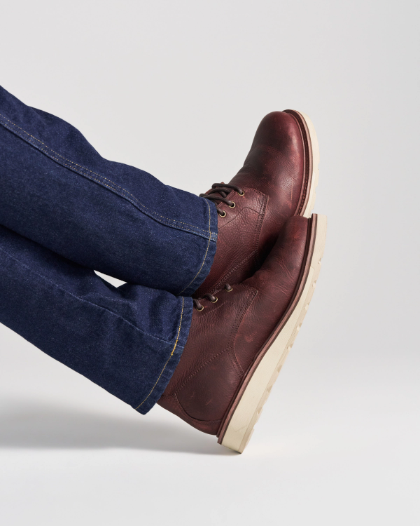 The Knox Lace Up in Cognac Cowhide. A person wearing dark blue jeans and cognac cowhide Knox lace-up boots with light-colored soles.