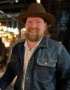 A bearded man wearing a denim jacket and hat.
