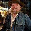 A bearded man wearing a denim jacket and hat.