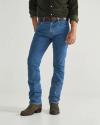 A person wearing a dark green shirt, blue jeans, brown belt, and brown boots stands against a plain background.
