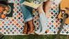 Two people sitting on a quilt with a guitar and vinyl records, showcasing their boots.