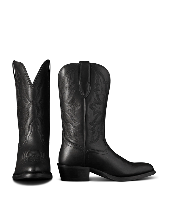 The Britt in Midnight Cowhide. Two black leather cowboy boots crafted from midnight cowhide with decorative stitching are shown; one boot faces forward, while the other is viewed from the side.