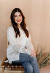 A woman in jeans and a white shirt sitting on a wooden chair.