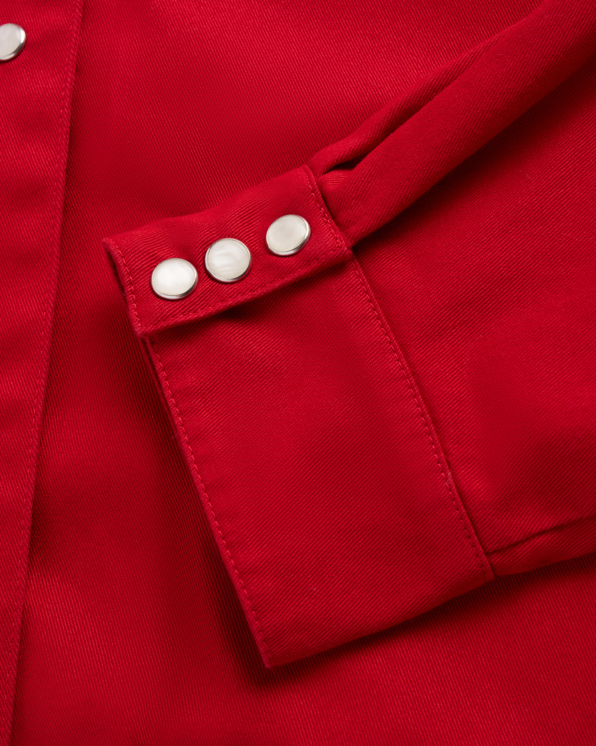 Close-up of a red fabric jacket sleeve with three silver snap buttons on the cuff.