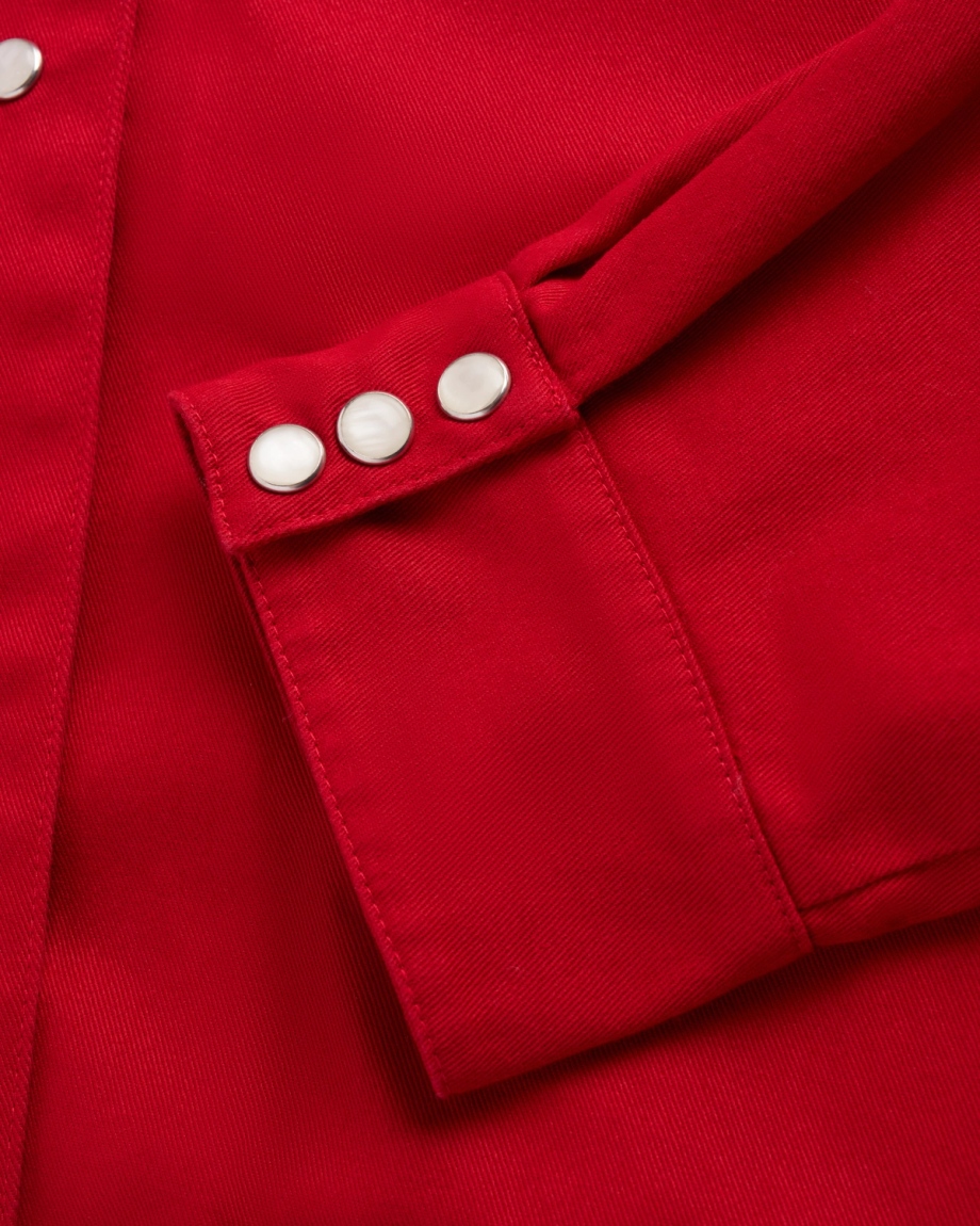 Close-up of a red fabric jacket sleeve with three silver snap buttons on the cuff.