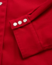 Close-up of a red fabric jacket sleeve with three silver snap buttons on the cuff.