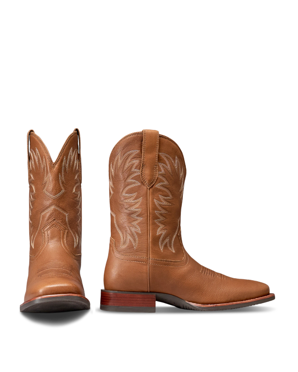 The Dusty in Mesa Goat. Pair of tan leather cowboy boots with decorative stitching, brown wooden heels, and pull straps—shown from side and front angles against a white background—crafted by The Dusty Goat for timeless Western style.