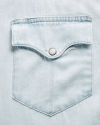 Close-up of a light blue denim shirt pocket with a flap and a metal snap button.