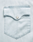 Close-up of a light blue denim shirt pocket with a flap and a metal snap button.