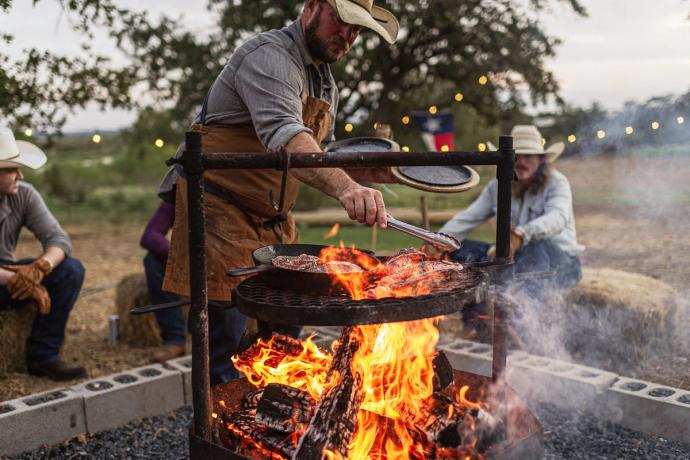 a man adjusting meat over a fire pit