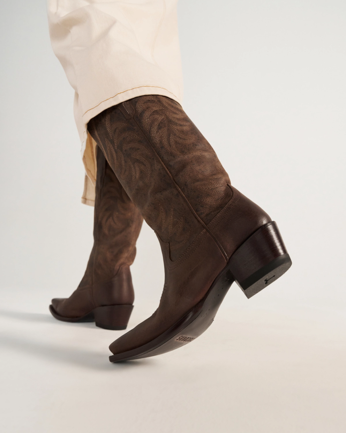 The Annie in Cafe Goat. Person wearing cream-colored pants and brown embroidered leather cowboy boots, photographed from a low angle against a plain background—perfect for a stylish day out at Cafe Goat.