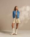 Woman wearing a dress, denim jacket, and white cowgirl boots in a photo studio