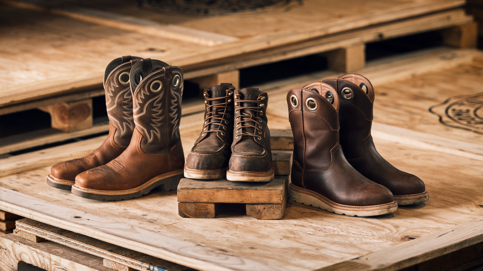 Three pairs of brown leather work boots displayed on wooden pallets.