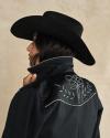 Person in a black cowboy hat and embroidered jacket faces away, holding the jacket collar up, with short dark hair visible.