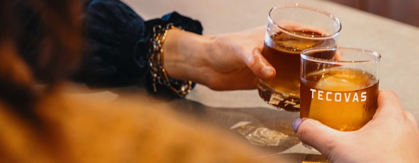 Two drinks labeled with Tecovas clinking together