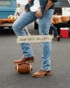 A person wearing jeans and brown boots stands with a foot on a football next to a tailgate area. Text overlay reads "Shop Best Sellers.