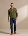 Man wearing jeans and slip ons with a green long sleeve in a photo studio