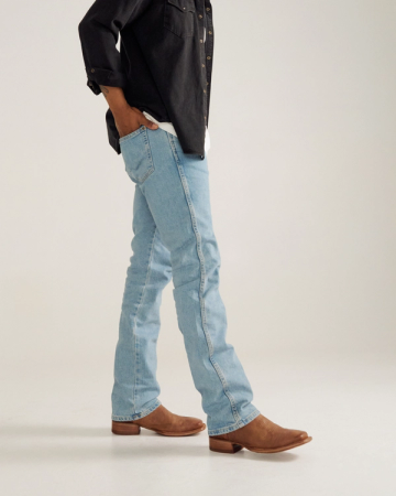 Person standing in light blue jeans, brown boots, and a dark long-sleeve shirt with hands in pockets against a plain background.