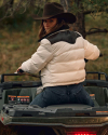 A person wearing a cowboy hat and white jacket sits on an all-terrain vehicle outdoors, looking back over their shoulder.