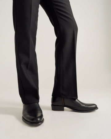 A person wearing black dress pants and black leather shoes stands on a light-colored surface.