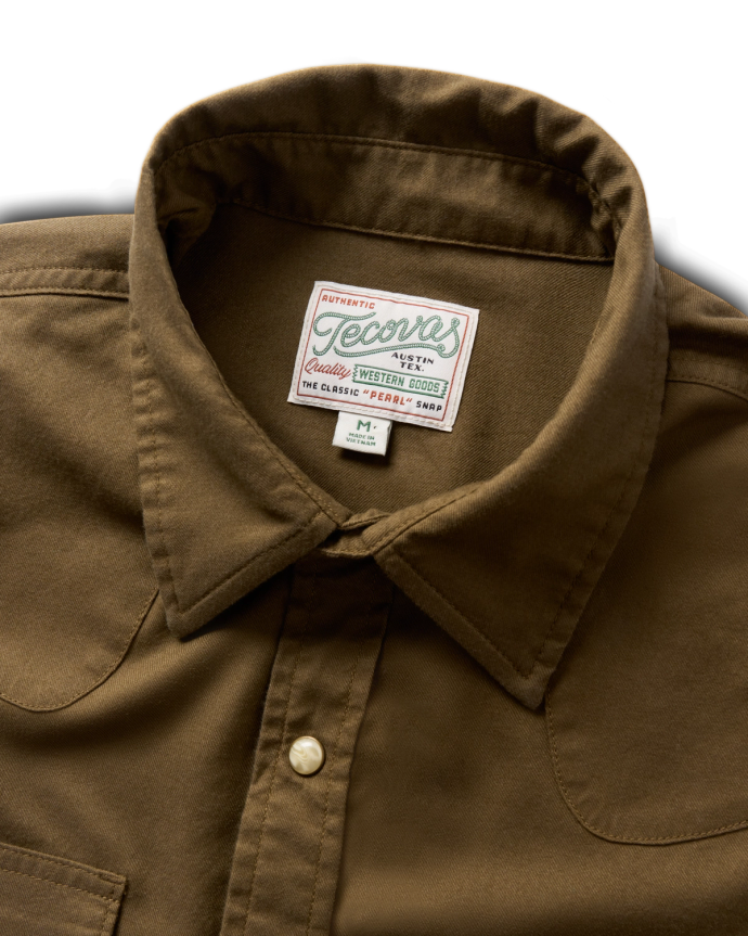 Close-up of a brown button-up shirt with a label reading "Tecovas" and "Classic Western Boots" sewn onto the inside collar.