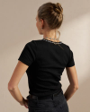 A person with a bun hairstyle is shown from the back, wearing a black ribbed short-sleeve top and dark pants, standing against a neutral background.