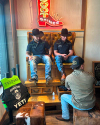 Two men in black cowboy hats sit in large leather chairs, getting their boots shined by a person kneeling in front. A neon sign shaped like a boot hangs in the background.