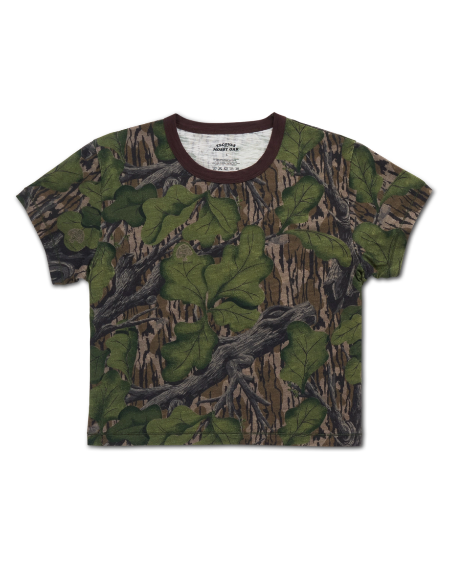 A short-sleeve t-shirt featuring a photorealistic forest camouflage pattern with green leaves, brown branches, and tree bark, displayed on a white background.