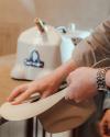 A person shapes a light-colored hat by hand near a steam machine on a countertop.