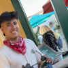 A young person with a red bandana is smiling, holding a torch tool. There are people and umbrellas in the background.