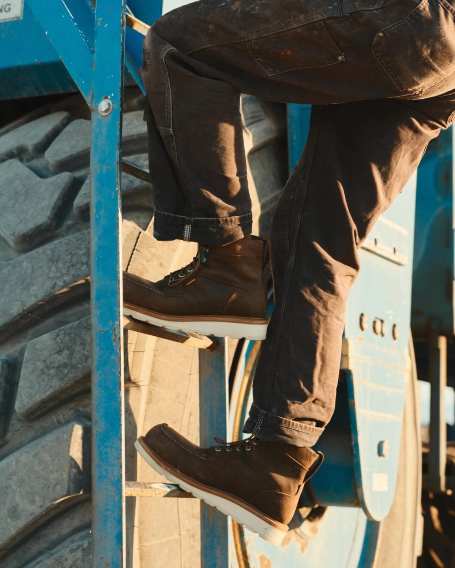 LongHaul Waterproof Moc Composite Toe Work Boot in Espresso Cowhide. Wearing cowhide work boots and dark pants, a person climbs a blue metal ladder attached to large industrial equipment with oversized tires.