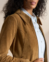 Close-up of a person wearing a light blue button-up shirt under a tan suede jacket, with wavy dark hair partially visible.