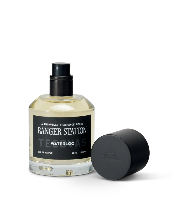 A bottle of Ranger Station Waterloo Eau de Parfum with a black spray nozzle and detached black cap placed beside it.