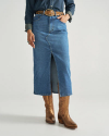 A person wearing a blue denim skirt with a front slit, a brown belt, a blue shirt, and brown cowboy boots stands against a plain background.