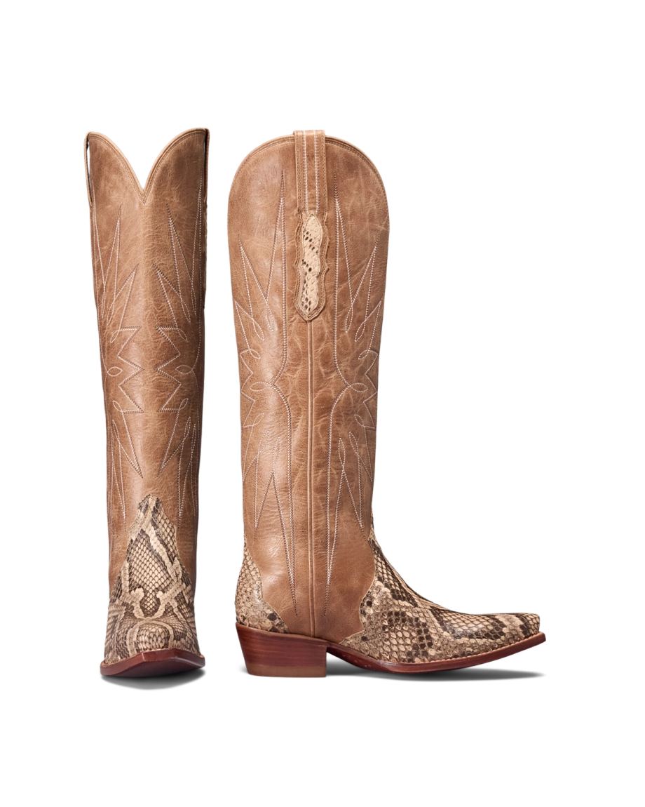 A pair of tall, tan cowboy boots with pointed toes, mangrove-toned snake print accents inspired by the Loretta Invasive Python, and stitched patterns on the leather shafts.