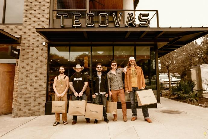 Five men standing in front of a tecovas store, each holding shopping bags, with a vintage filter effect.