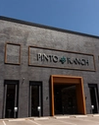 Exterior view of the Pinto Ranch store with a brick facade, large sign, and orange-framed entrance under a clear blue sky.