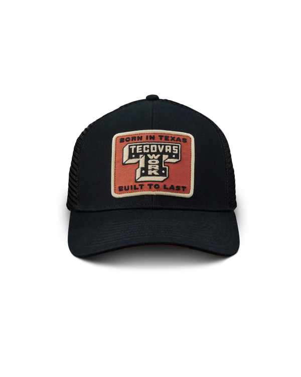 A black mesh trucker hat with a rectangular patch reading "Born in Texas Tecovas Built to Last" in tan, white, and orange colors.