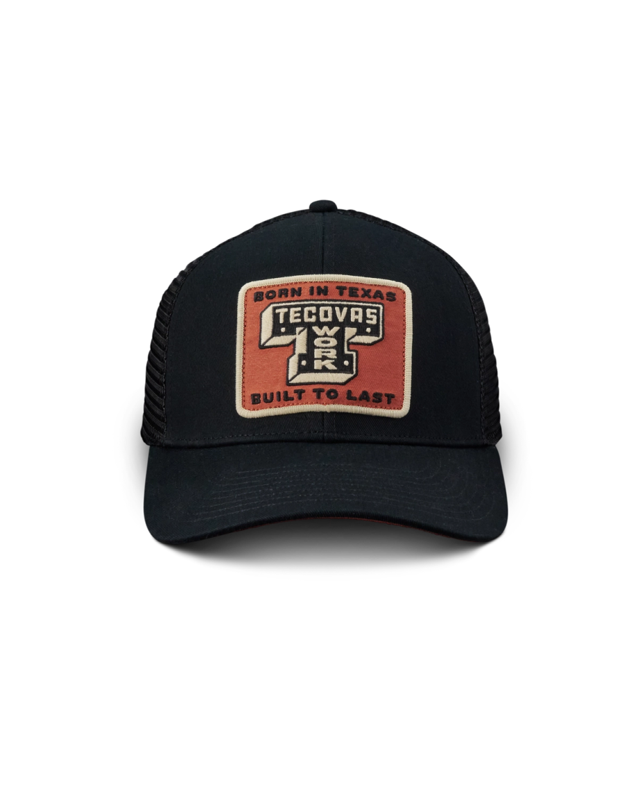 A black mesh trucker hat with a rectangular patch reading "Born in Texas Tecovas Built to Last" in tan, white, and orange colors.