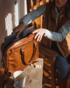 Woman putting a laptop into the Bartlett Slim Briefcase in Cognac