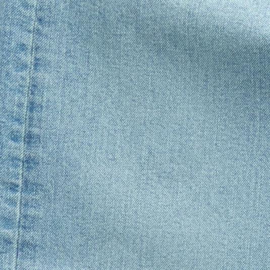 Close-up of light blue denim fabric showing a seam with visible stitching on the left side.